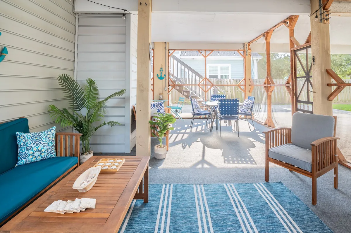 A welcoming living space featuring a blue couch with decorative pillows, a wooden coffee table, a striped area rug, and a view of an outdoor dining set through glass doors. The room is bright, casual, and ideal for group relaxation or shared activities.