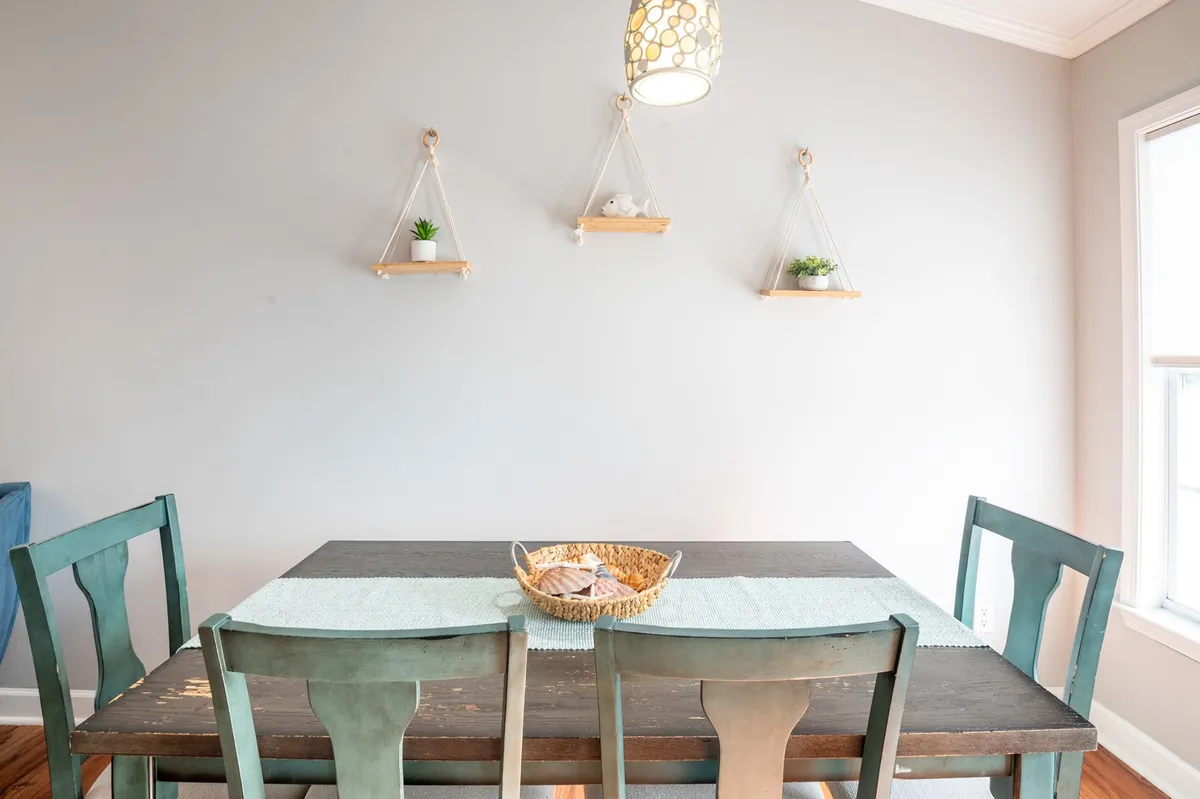 A cozy dining area with a wooden dining table, hanging plants, a stylish light fixture, and a decorative centerpiece. The setup is inviting, ideal for both intimate family meals and lively group gatherings.