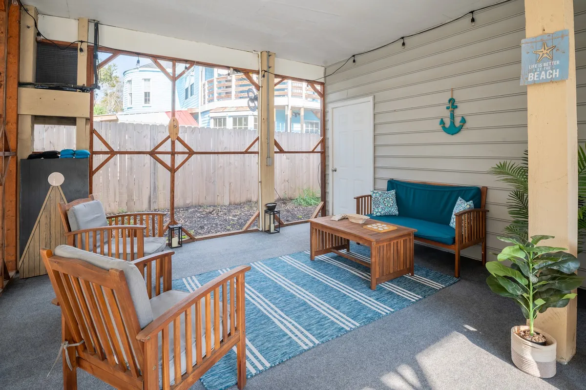 A cozy, casual seating area on a screened porch with wooden chairs, a coffee table, and nautical decor, including an anchor on the wall. The setting feels intimate and is softly lit, ideal for evening gatherings with friends or quiet coffee mornings with a view.