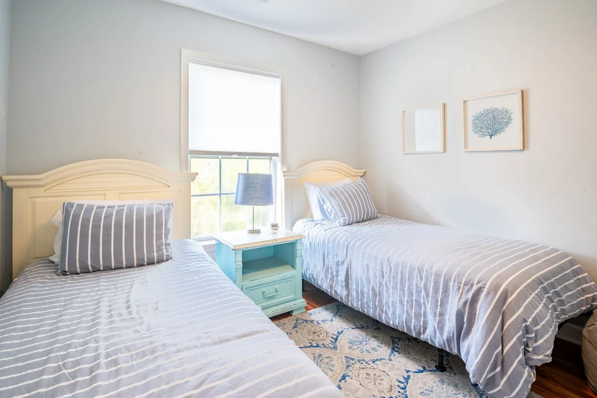 A cheerful twin bedroom with two twin beds, a bedside table, and decorative wall art. The room is filled with natural light, giving it a bright and welcoming feel perfect for children.