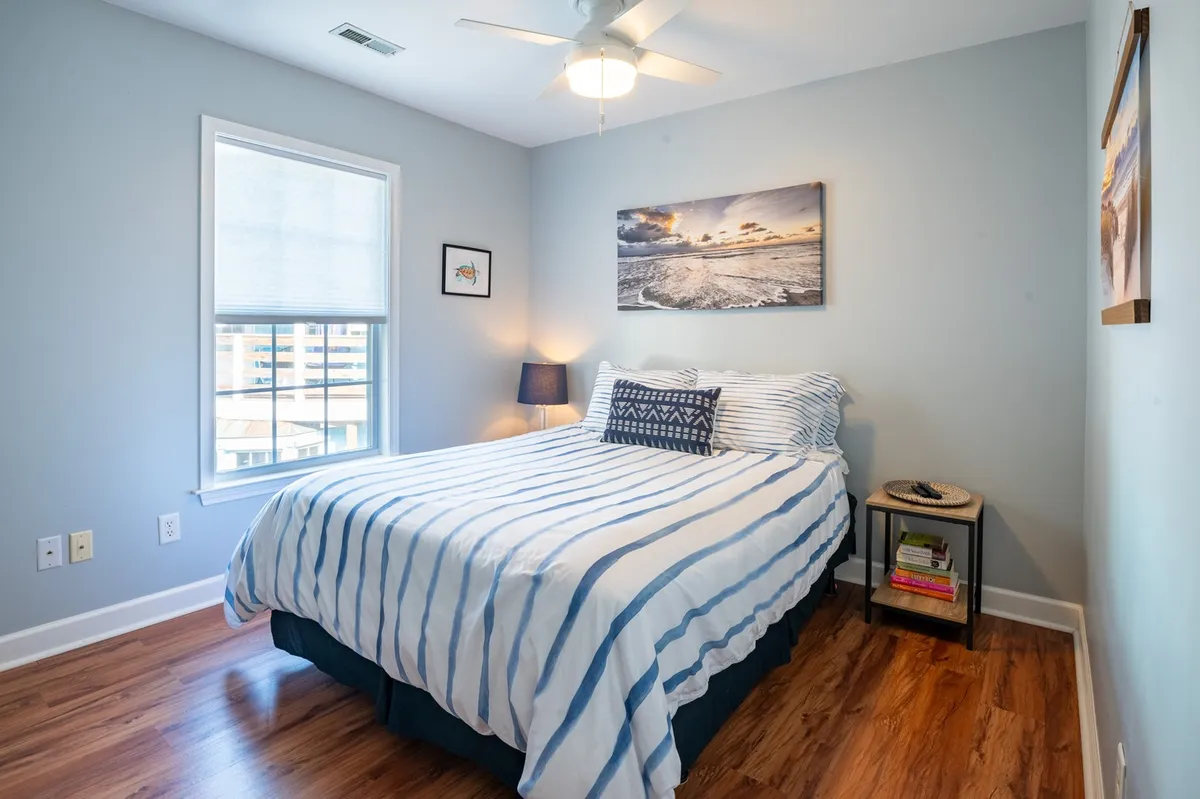 A tranquil bedroom with a striped bed, wall art, and a lamp on the nightstand. The room feels restful and bright, ideal for unwinding after a day of coastal adventures.