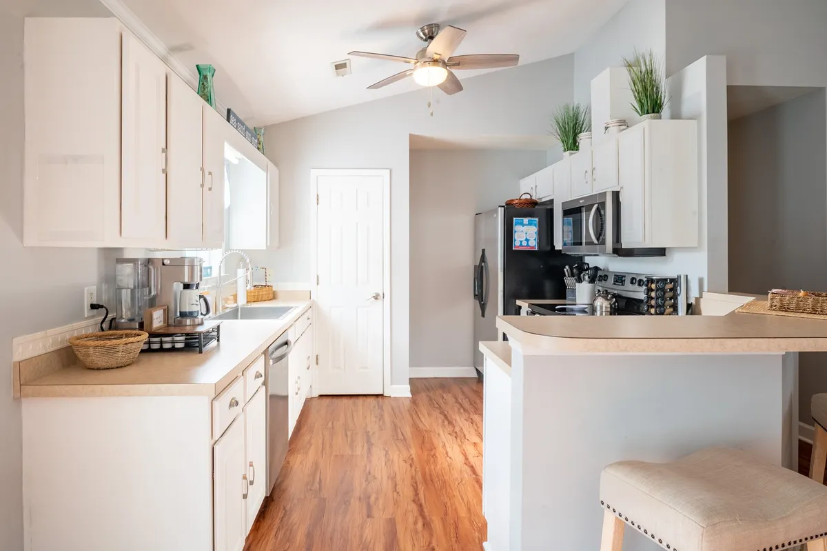 A modern kitchen with a central island, stainless steel appliances, ample countertop space, and wood flooring. The island serves as a gathering spot for meal prep or casual dining, with appliances and fixtures emphasizing the kitchen’s functionality and style.