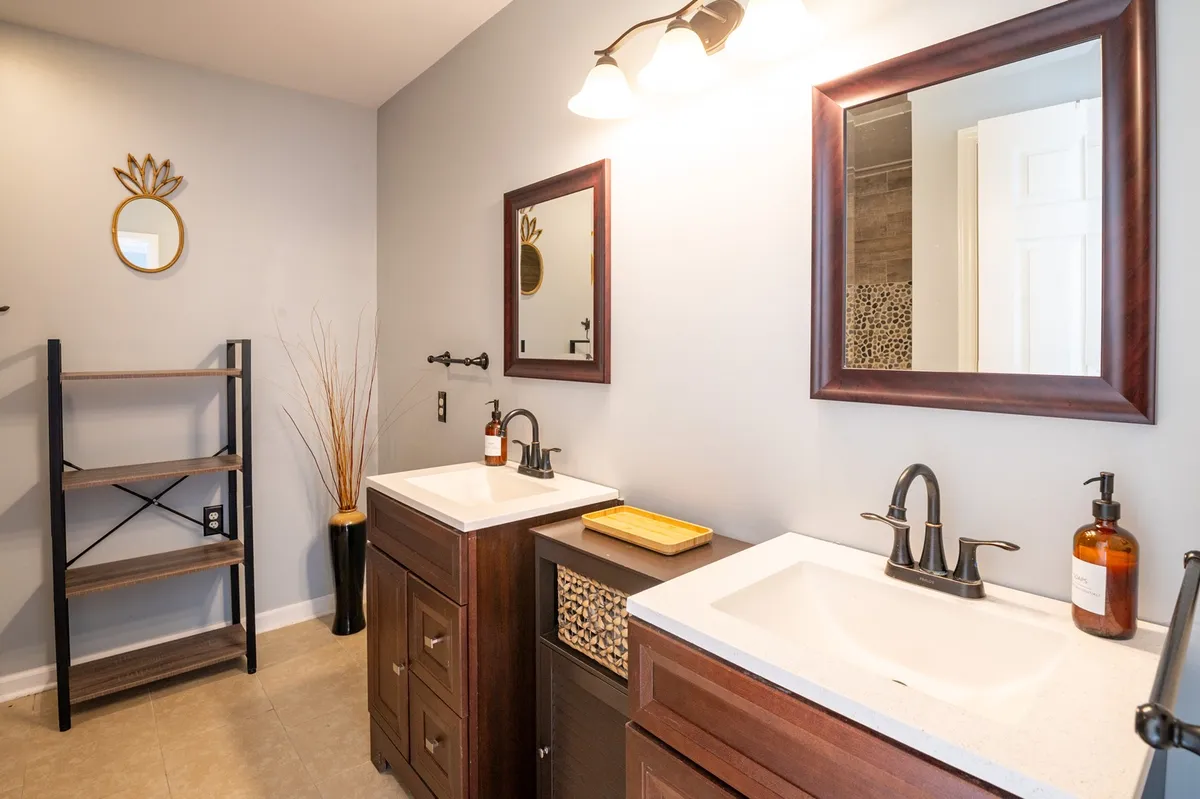 A modern bathroom with a double sink vanity, mirrors, and a wooden shelving unit. The space exudes cleanliness and functionality, ideal for family routines and self-care.