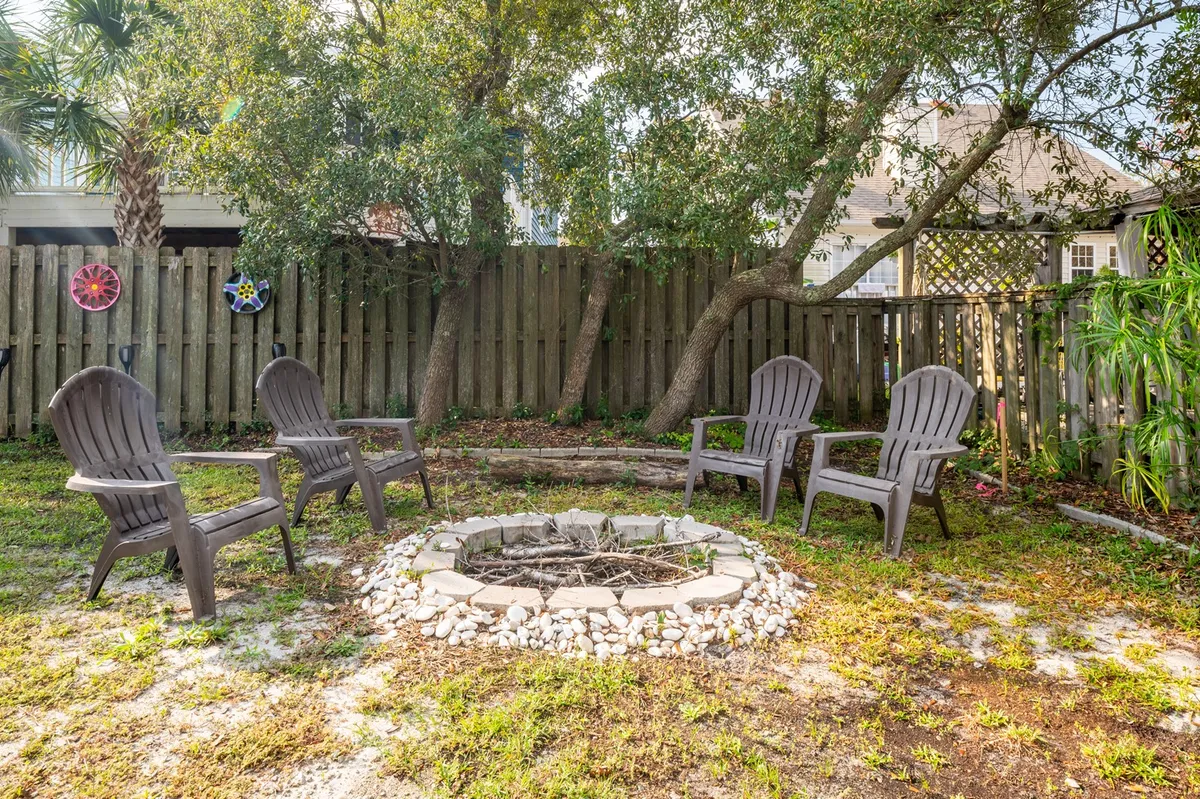 A cozy backyard fire pit surrounded by Adirondack chairs, set against a backdrop of tall trees. The scene invites families to gather in the evening for marshmallow roasting, storytelling, and stargazing under the night sky.