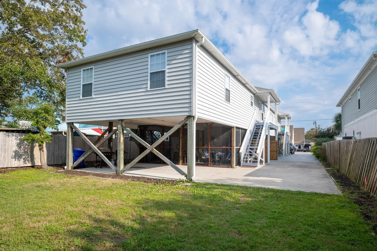 The home’s exterior in full daylight, featuring its elevated construction and a spacious, grassy backyard. Children are pictured playing on the lawn, while the clear sky and ample outdoor space highlight opportunities for backyard games, barbecues, and outdoor family gatherings.